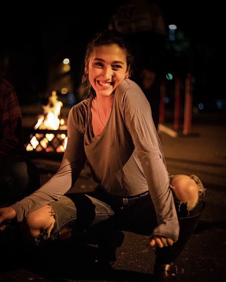 girl sits smiling, cross-legged, in front of fire pit