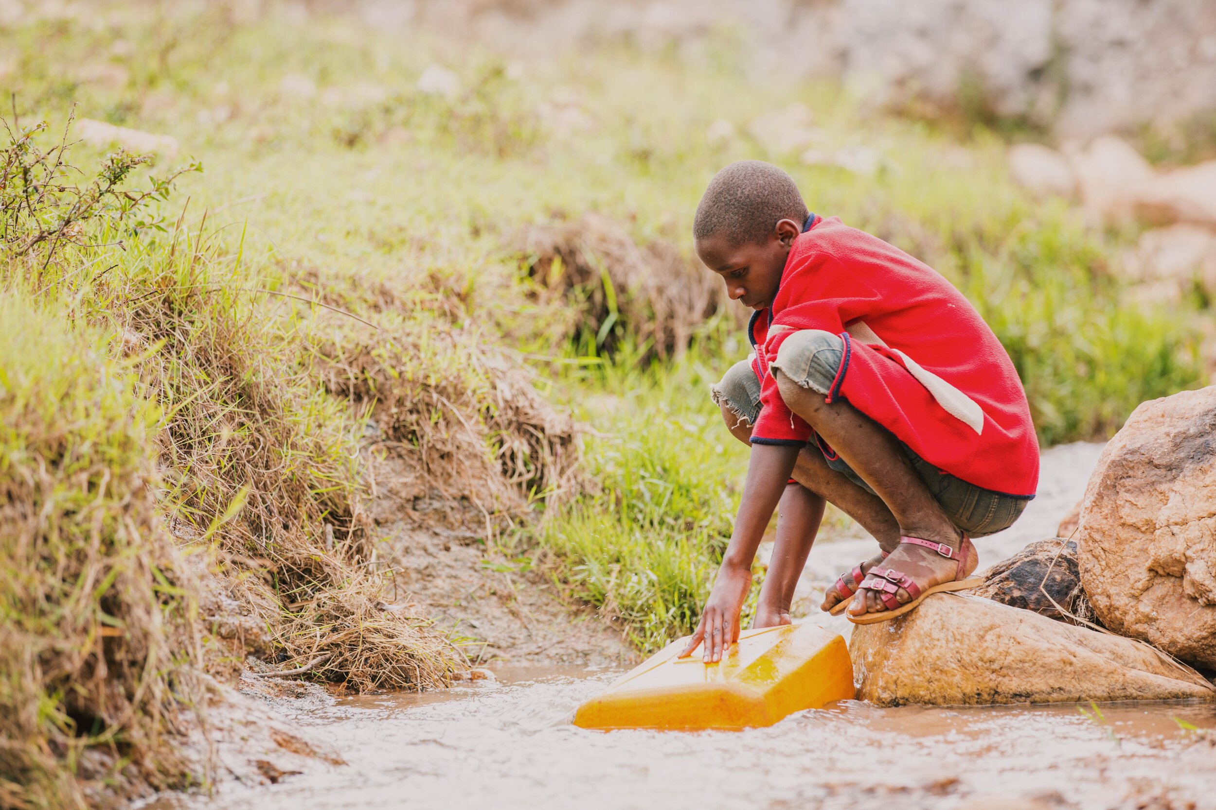 boy draws water from a stream