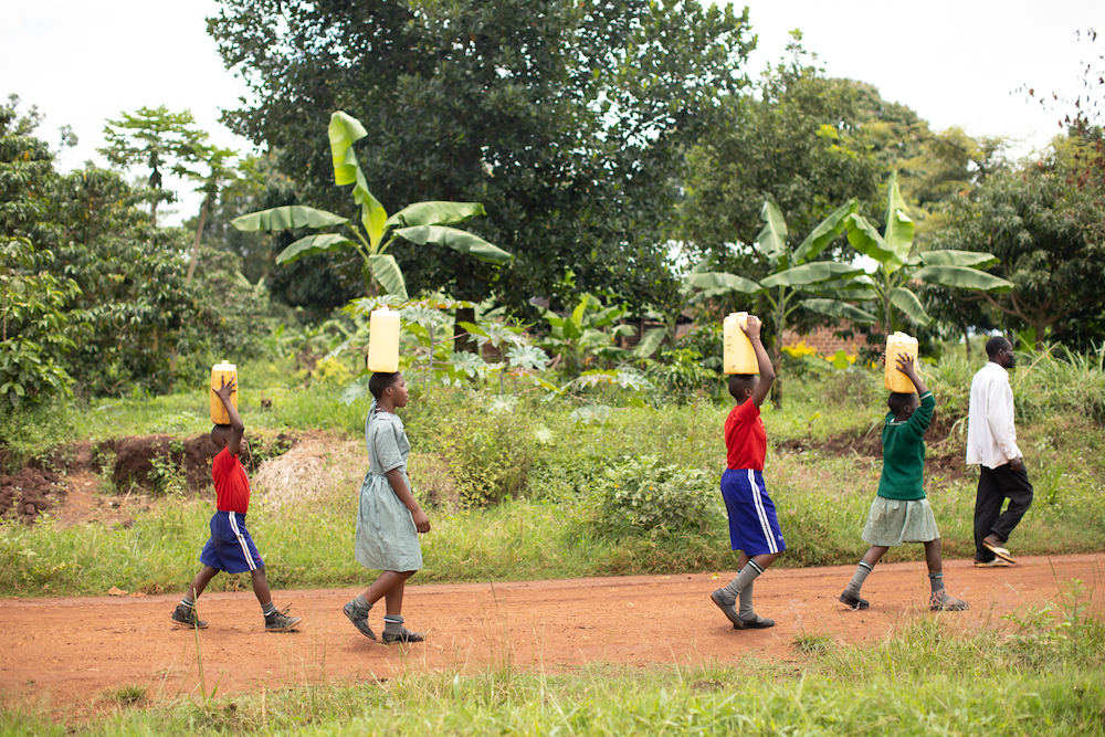 African students walking with jerrycans full of water on their heads