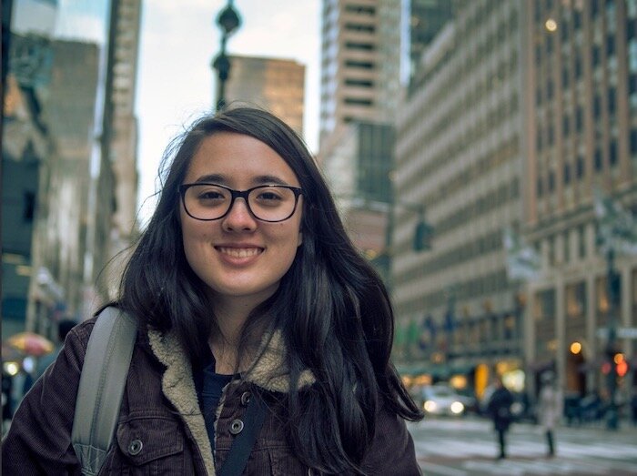 girl with glasses smiles at camera with a city street in the background