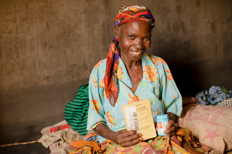 woman wearing a red scarf on her head smiles while holding her HIV medication