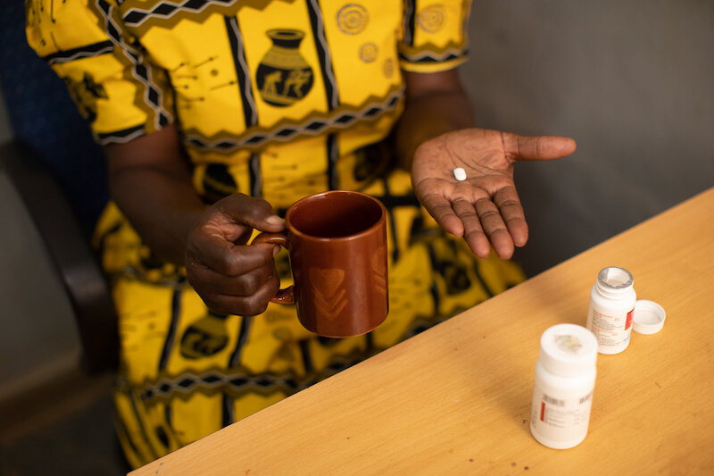 woman in a yellow dress holds a mug and hiv medication in her hands
