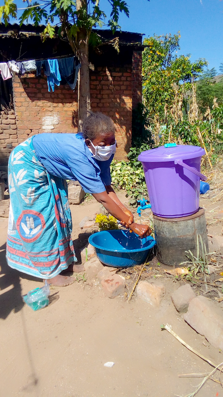 Woman in face mask washing hands using tapped plastic container and basin as precautionary measure to COVID-19