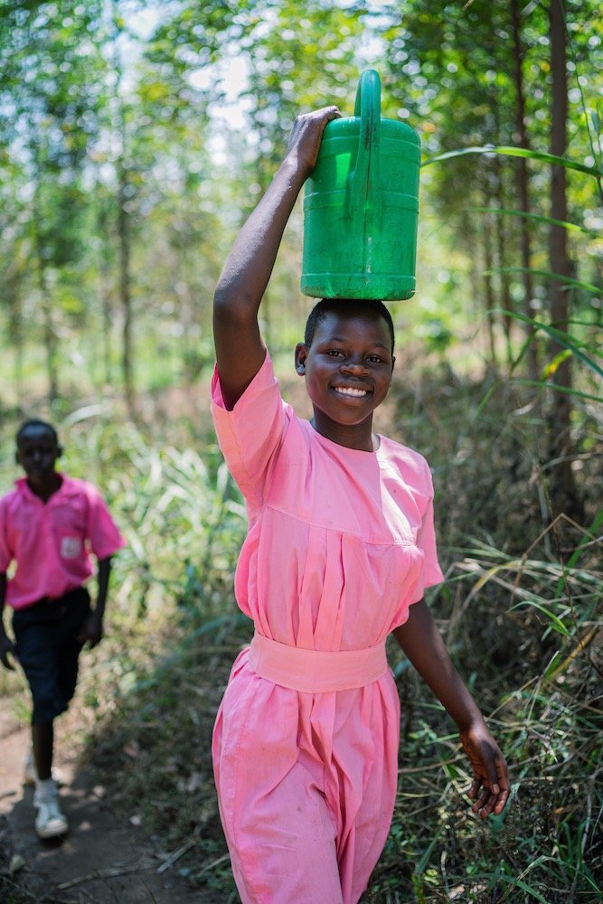 ugandan girl in school uniform, carrying water on her head