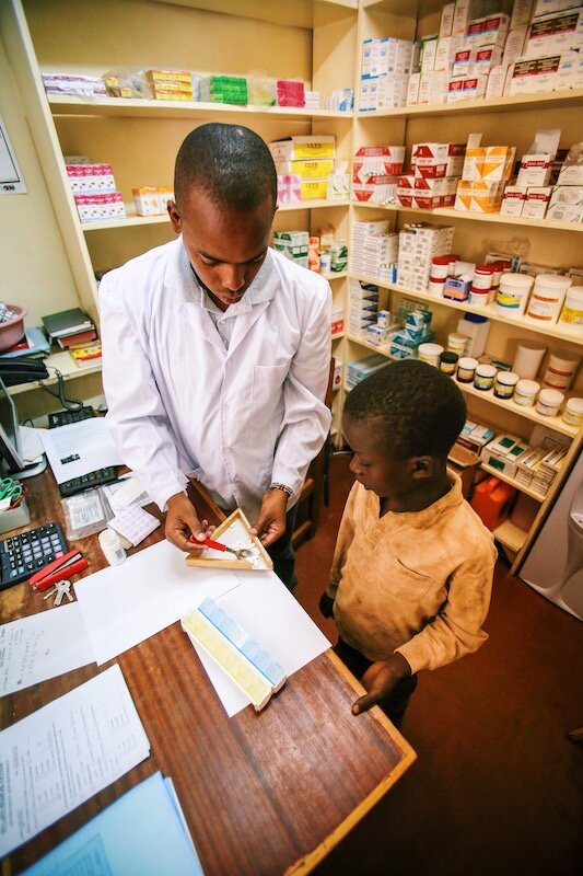 health worker shows a young boy how he scoops medicine