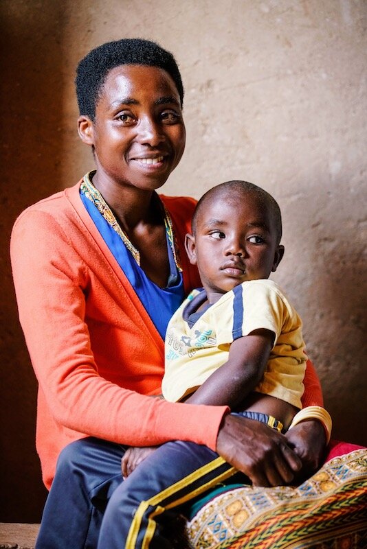 mother wearing an orange and blue shirt holds her child on her lap while smiling