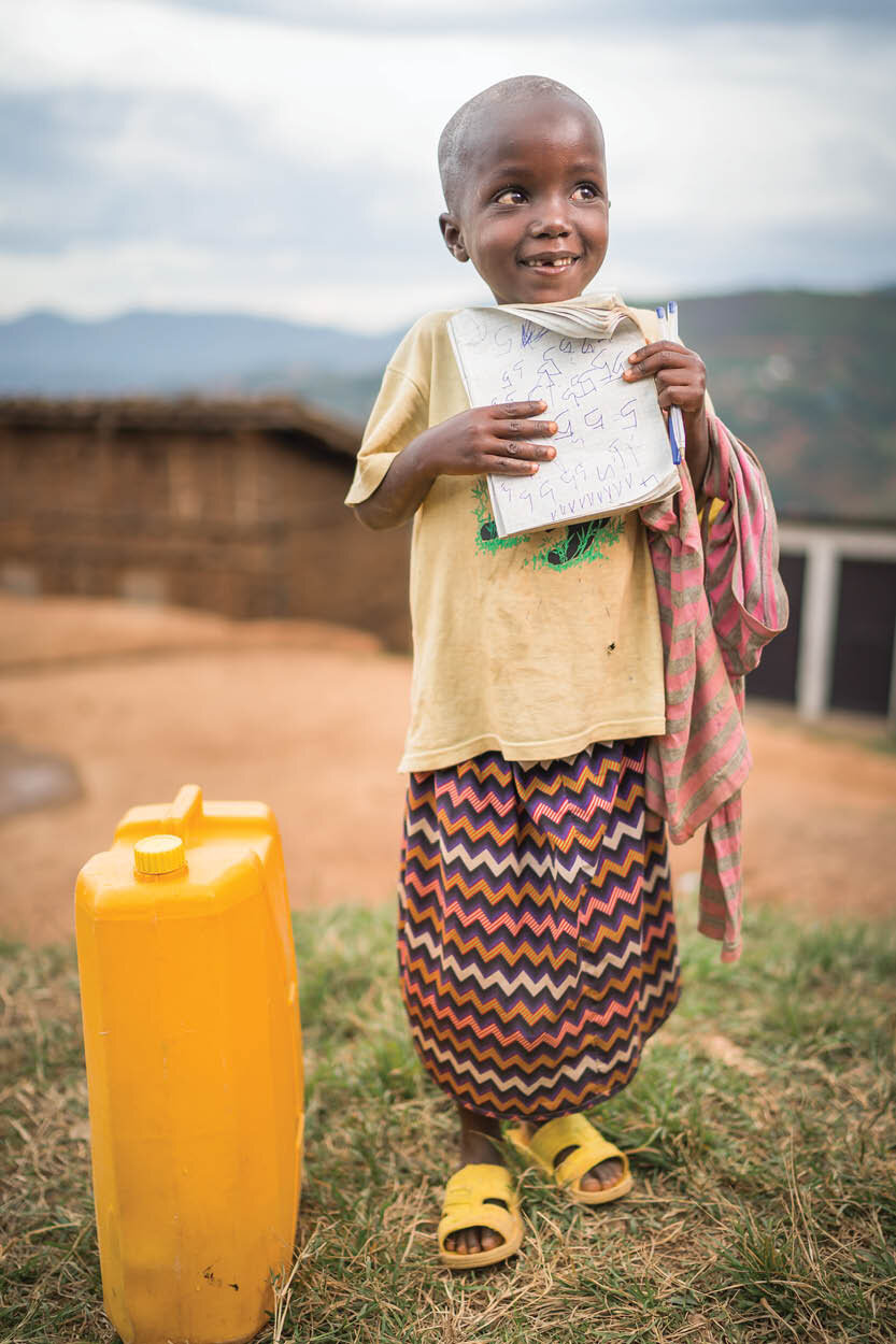 young african girl stands holding her school notebook with a jerrycan next to her