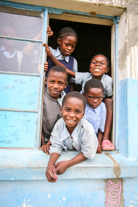 Group of african children looking out a window and smiling