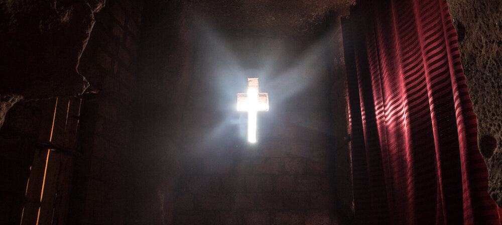 sunlight shining through a cross cutout in a wall