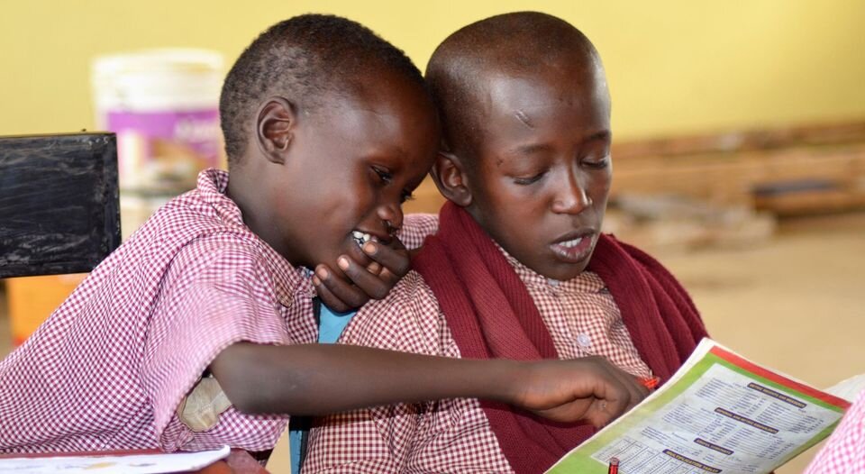 two african children look at a book together
