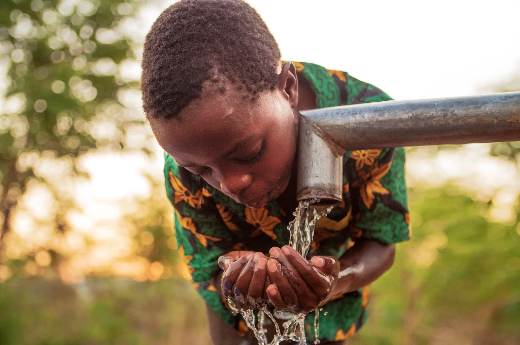 african child cups clean water flowing from a pipe