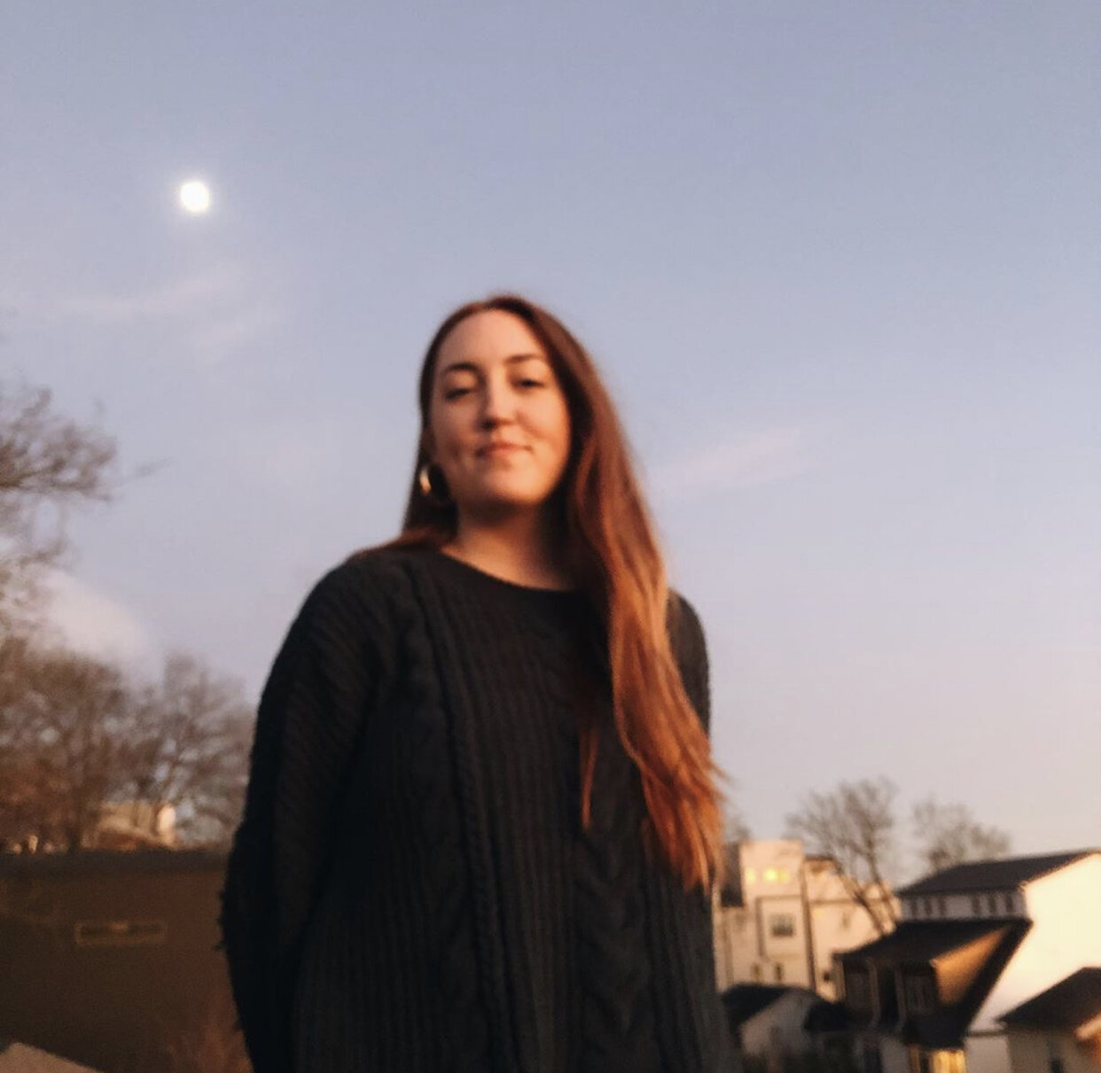 girl in sweater smiles at camera, moon shines behind her