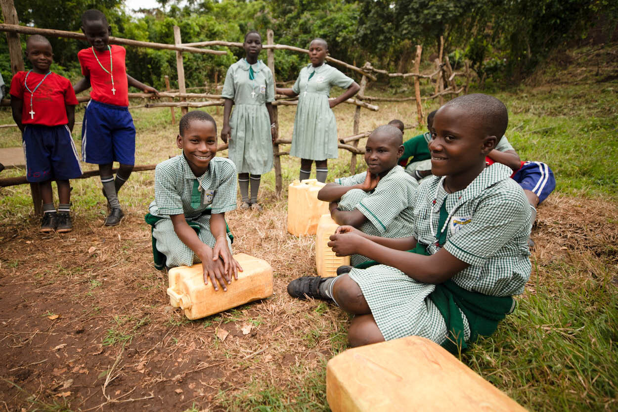 schoolchildren sit with their jerrycans waiting to fill them with water before returning to class