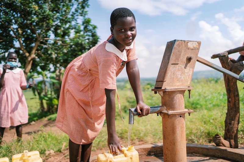 girl filling jerry can with water from well