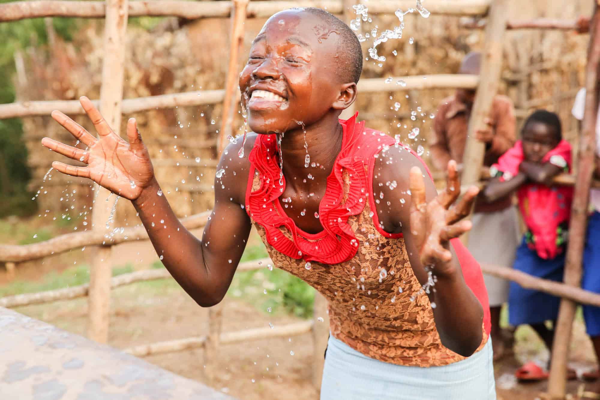 A smiling African youth splashing their face with water